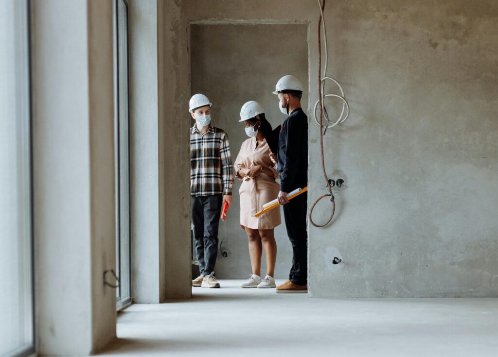 Realtors and clients wearing hard hats exploring a modern construction site indoors.